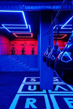 an indoor gym with blue and red lighting on the ceiling, two exercise machines in the foreground