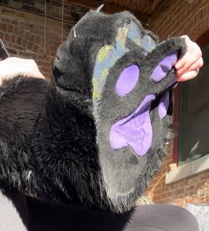 a person wearing a furry animal mask on top of their head and hands in front of a brick building