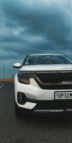 a white car is parked on the side of the road with dark clouds in the background