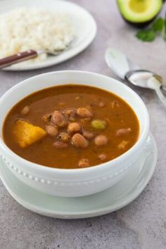 a white bowl filled with beans and rice next to an avocado on a table