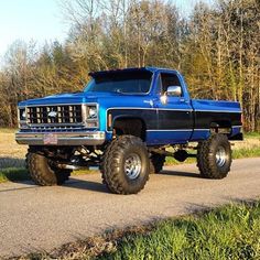 a large blue truck parked on the side of a road next to grass and trees