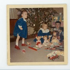 an old photo of two children and their toys in front of a christmas tree with presents on the floor