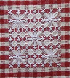 a red and white checkered table cloth with small flowers on the center, along with two rows of stitches