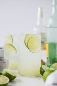 two glasses filled with lemonade and limes next to each other on a table