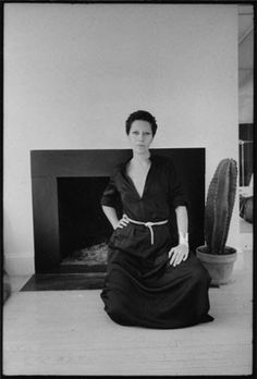 an old photo of a woman sitting in front of a fireplace with her hands on her hips