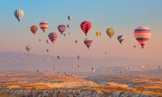 many hot air balloons are flying in the sky over mountains and deserts at sunrise