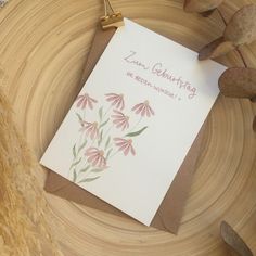 a card with flowers on it sitting on top of a wooden table next to some rocks