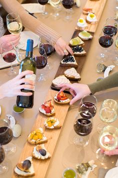 several people sitting at a table with wine and food on it, while one person holds a bottle of wine in the other hand