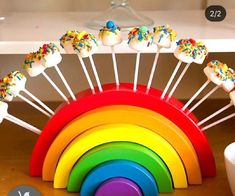 a rainbow cake pops with sprinkles sitting on top of a wooden table