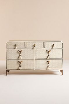 a white dresser with gold handles and knobs on the top, against a beige wall