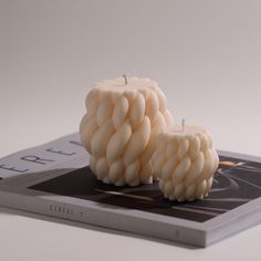 two white candles sitting on top of a book next to it's cover,