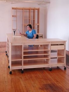 a woman sitting at a desk in an empty room with shelving on the wall