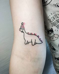 a woman's arm with a small tattoo of a dinosaur wearing a party hat