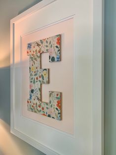 the letter e is made out of paper and framed in a white frame with flowers on it