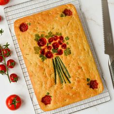 a cake with tomatoes and herbs on it sitting on a cooling rack next to a knife