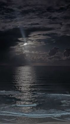 the moon is shining over the ocean on a cloudy night with waves crashing in front of it