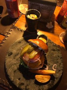 a large hamburger sitting on top of a stone plate next to fries and pickles