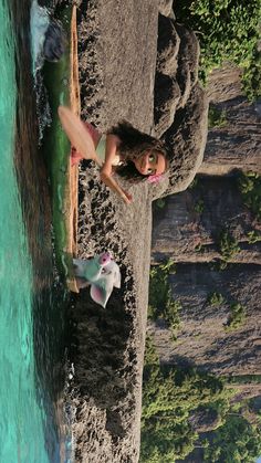 a woman standing on top of a beach next to a body of water and trees