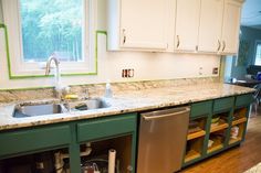 a kitchen with green cabinets and white counter tops, an open dishwasher in the middle