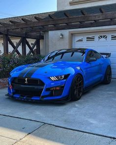 a blue sports car parked in front of a house with a garage door and driveway