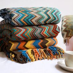 a stack of blankets sitting on top of a table next to a cup and saucer