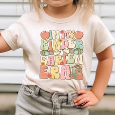 Step into the school year with flair with our 'In My Kindergarten Era' shirt, a retro-inspired tee perfect for your little one's big step into kindergarten. This charming design combines nostalgia with the excitement of starting school, making it the perfect back-to-school outfit for your kindergartner. Designed to celebrate this new chapter, our Kinder Tee is as comfortable as it is cute, ensuring your child feels great on their first day and beyond. Available in designs suited for both boys and girls, it's the ideal way to make school beginnings memorable and stylish! How to Order 1. Select Size: Choose the right size from the size chart provided in the photos. 2. Choose Color & Style: Select your preferred color. Decide between a crewneck or a hooded style for sweatshirts. 3. Pick Threa Kids First Day Of School, Kindergarten Outfit, Kindergarten Teacher Shirts, Back To School Kids, First Day Of School Outfit, Starting School, School Tees, Kindergarten Teacher, Back To School Outfits