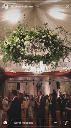 a group of people standing in front of a white tent with flowers hanging from the ceiling