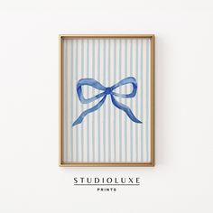 a painting with a blue bow on it in a gold frame against a white wall