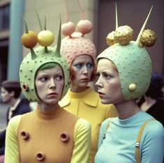 three women wearing weird hats in front of a building