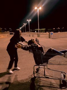 a woman pushing a man sitting in a shopping cart on the side of an empty street at night