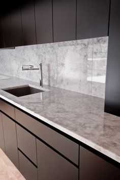 a kitchen with marble counter tops and black cabinets in the back drop off sink area