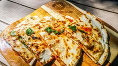 a wooden cutting board topped with sliced up pizza