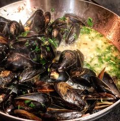 a pan filled with mussels and broccoli on top of a stove