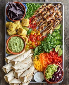 a platter filled with chicken, vegetables and tortillas