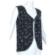 Weighing nearly three pounds, every square inch of this remarkable vest is covered--in some areas up to a half an inch high--in enormous faceted beads, sequins or bugle beads. And though the vest is predominantly black, the aurora borealis finish on assorted sequins also casts shards of green, blue and purple light at certain angles. Like a wearable chandelier! Collarless sweetheart V-neck vest of wool knit crusted with lattice-pattern faceted beads, bugle beads and sequins. Cutaway front hemlin Concert Style, Long Sleeve Evening Gowns, Concert Fashion, Chandelier Crystal, The Aurora Borealis, Tassel Dress, Beaded Neckline, The Aurora, Purple Light