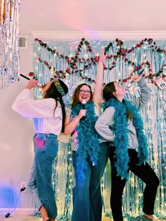 three girls are posing for the camera with their arms in the air and one girl is wearing a blue feather boa