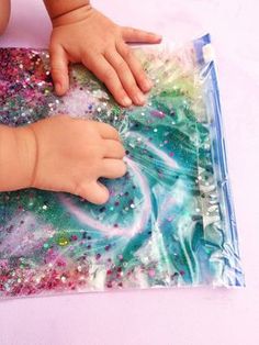 a baby's hand on top of a plastic bag filled with colorful liquid and glitter