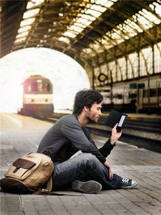 a man sitting on the ground with a book in his hand and a train passing by