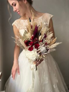 a woman in a wedding dress holding a bouquet with dried flowers and feathers on it