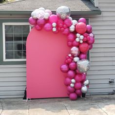 a pink arch decorated with balloons in front of a house