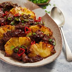 a plate filled with pineapples and meat on top of a table next to a spoon