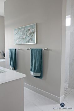 a white bathroom with blue towels hanging on the wall and marble counter tops in front of it