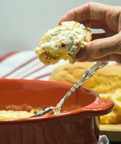 a hand holding a piece of food over a red bowl