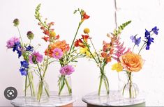 three vases filled with colorful flowers on top of marble bases in front of a white wall