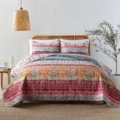 a bed covered in a colorful comforter next to a lamp and potted plant