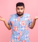 a man with his hands out in front of him on a pink background wearing a blue shirt