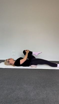 a woman in black shirt and leggings doing yoga on white mat with grey carpet