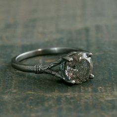 a close up of a diamond ring on a wooden surface with the center stone missing