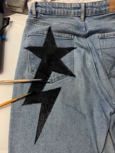 a pair of jeans with an image of a star painted on the side and two pencils next to it