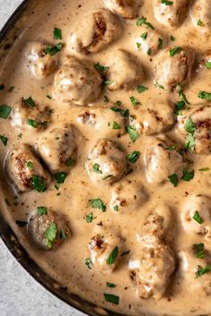 a skillet filled with meatballs covered in gravy and garnished with parsley